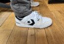 The Converse CL 98 in white grey black on feet worn with grey pants on hardwood floor