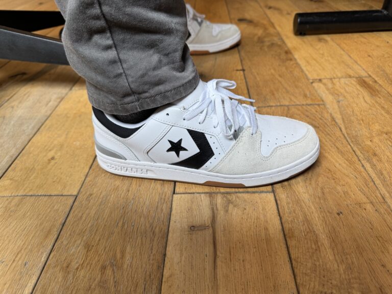 The Converse CL 98 in white grey black on feet worn with grey pants on hardwood floor