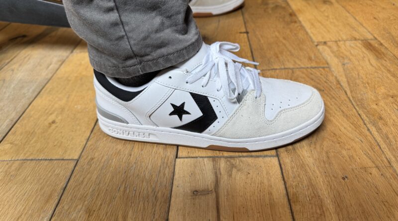 The Converse CL 98 in white grey black on feet worn with grey pants on hardwood floor